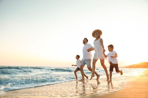 Glückliche Familie läuft am Sandstrand in der Nähe des Meeres bei Sonnenuntergang